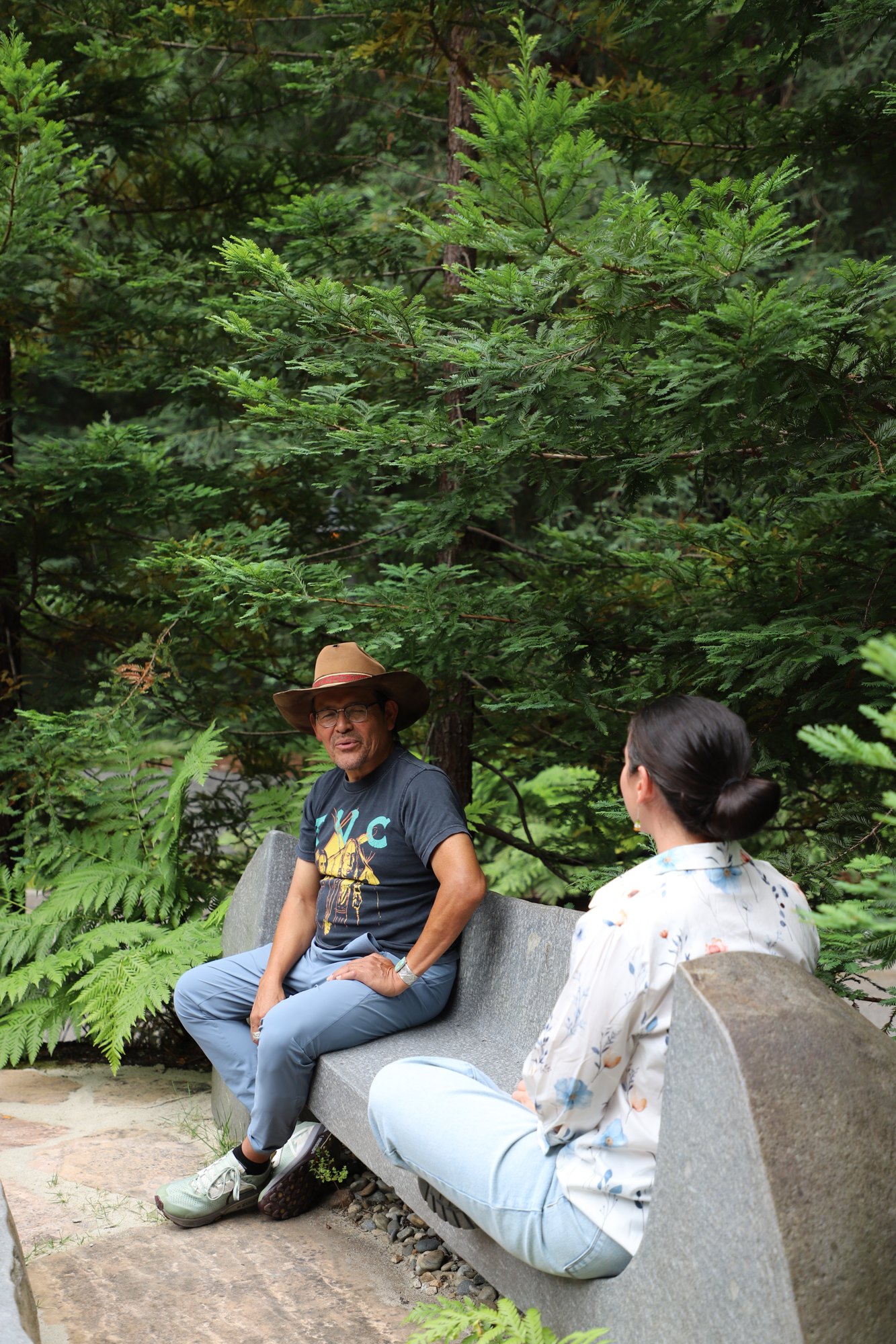 Two people talking on the stone bench under the redwoods at 1440
