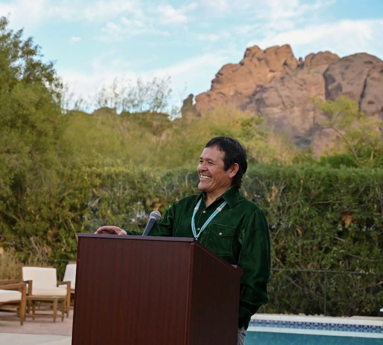 Tony Skrelūnas speaking at a gathering, red rocks behind him